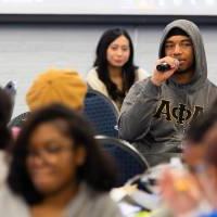 student with microphone asking question while seated at table